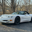Load image into Gallery viewer, A white C5 1997 through 2004 C5 Corvette convertible sports car parked outdoors on a paved surface with bare trees in the background.  Knightdrivetv round sleepy eye headlights and bezel installed
